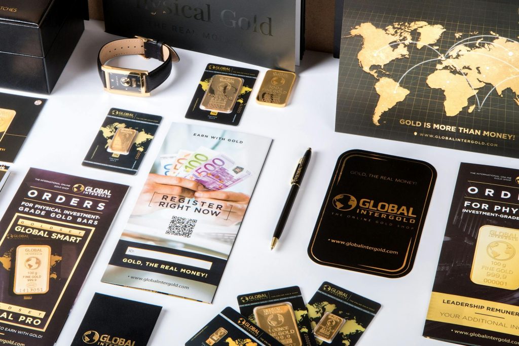 【EMU优化】广告投放中EMU还能做吗?如何优化?缩略图 Flat lay of promotional materials for gold investment, featuring brochures, cards, and gold bars.